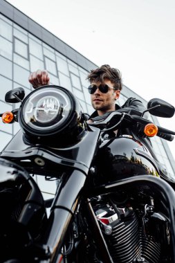 motosiklet üzerinde otururken uzağa bakan güneş gözlüğü ve deri ceket yakışıklı genç adam düşük açılı görünümü