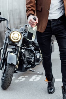 motosiklet yakınında yürüyüş ve alkol şişesi tutan kahverengi ceketli adam kırpılmış görünümü 