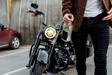 ceketli adamın kırpılmış görünümü motosikletten inip bir şişe alkol tutarak 