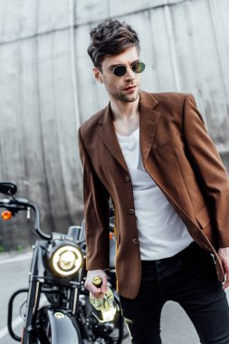 motosiklet yakınında alkol şişesi ile yürüyüş güneş gözlüğü ve kahverengi ceket yakışıklı adam seçici odak 