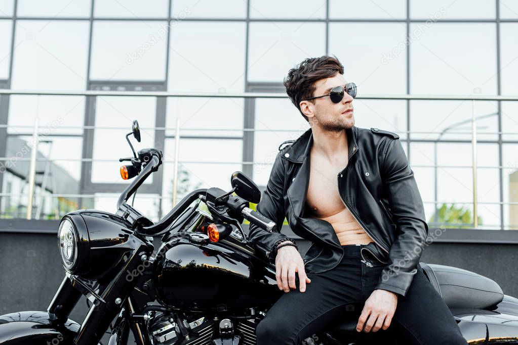 shirtless young man with muscular torso sitting on motorcycle and looking away