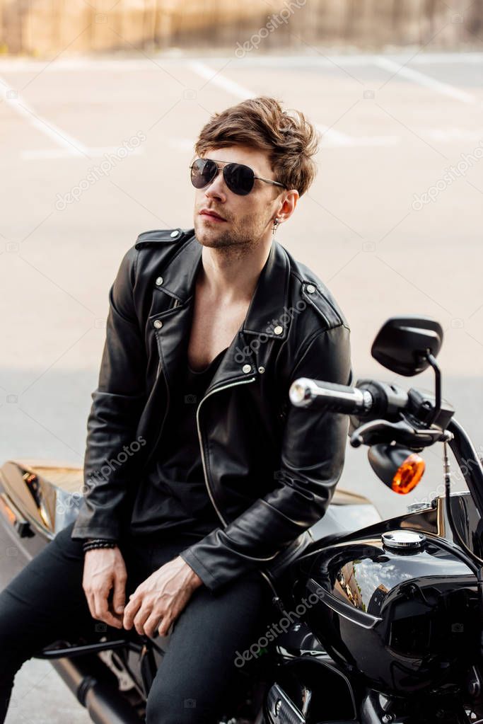 motorcyclist in leather jacket sitting on black motorcycle and looking away