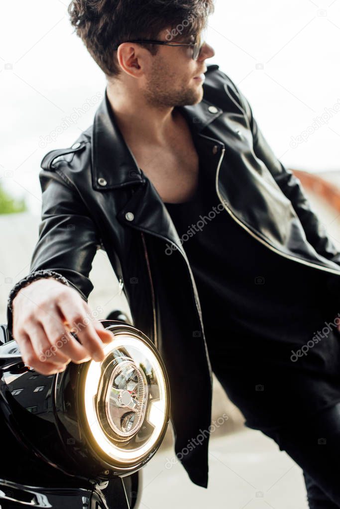 selective focus of light lamp of motocycle and handsome man in sunglasses standing near motorcycle