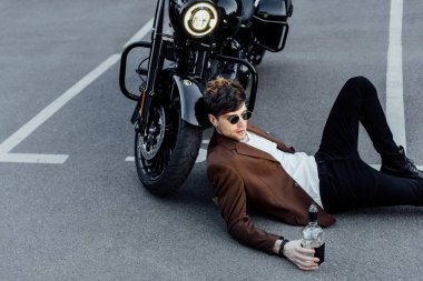 yakışıklı adam yerde yatarken alkol ile şişe tutan ve motosiklet tekerleği üzerinde baş eğilerek 