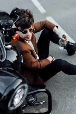 yakışıklı adam yeni motosiklet yakınında gorund oturan ve şişe tutan yüksek açı görünümü