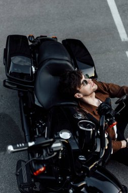 gözlük ve kahverengi ceket genç adam yerde otururken dinlenme ve motorcyce üzerinde eğilerek