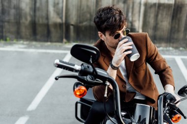 Kahverengi ceketli yakışıklı adam kağıt bardaktan kahve içiyor