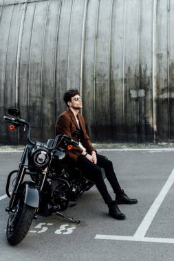 motosiklet üzerinde oturan motosikletçi iyon kahverengi ceket tam uzunlukta görünümü, dinlenme ve uzağa bakarak 