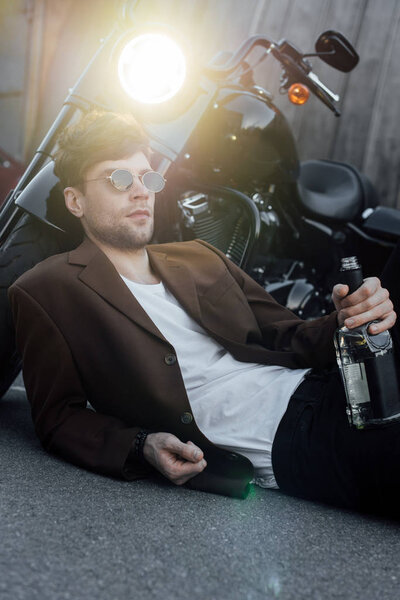 молодой человек лежит на земле рядом с мотоциклом со светящейся лампой
 