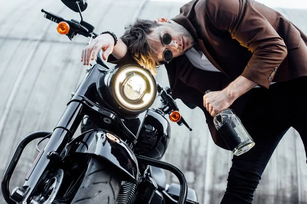 Młody Człowiek Pochylony Głowę Kierownicy Motocykla Lampką Trzymając Butelkę Alkoholem — Zdjęcie stockowe