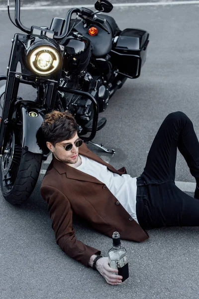 英俊的年轻人戴着太阳镜躺在地上 靠近摩托车用发光灯 — 图库照片