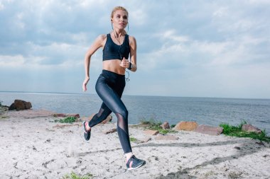 sportif sarışın kadın çalışan ve deniz kenarında kulaklıkmüzik dinleme 
