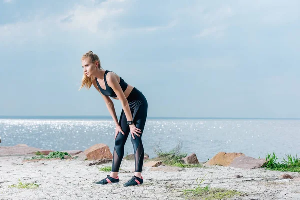 ผู้หญิงนักกีฬาที่น่าสนใจและเหนื่อย ยืนอยู่บนชายหาดใกล้ทะเล — ภาพถ่ายสต็อก