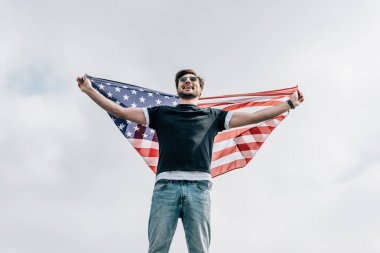 Gözlüklü yakışıklı adam Amerikan bayrağı tutarak ve çatıda gülümsüyor 