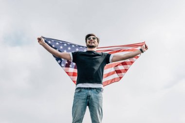 handsome man in glasses holding american flag and smiling on roof  clipart
