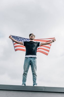 Gözlüklü yakışıklı adam Amerikan bayrağı tutarak ve çatıda gülümsüyor 