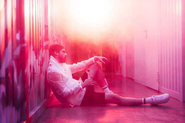 вид сбоку на красивого человека, сидящего на полу и держащего бутылку
 