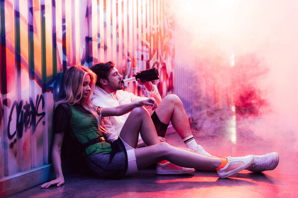 привлекательная блондинка сидит на полу, а красивый мужчина пьет шампанское
