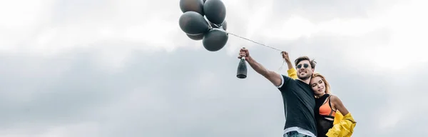 ボトルを持つ男と風船を持つ魅力的な女性のパノラマショット — ストック写真