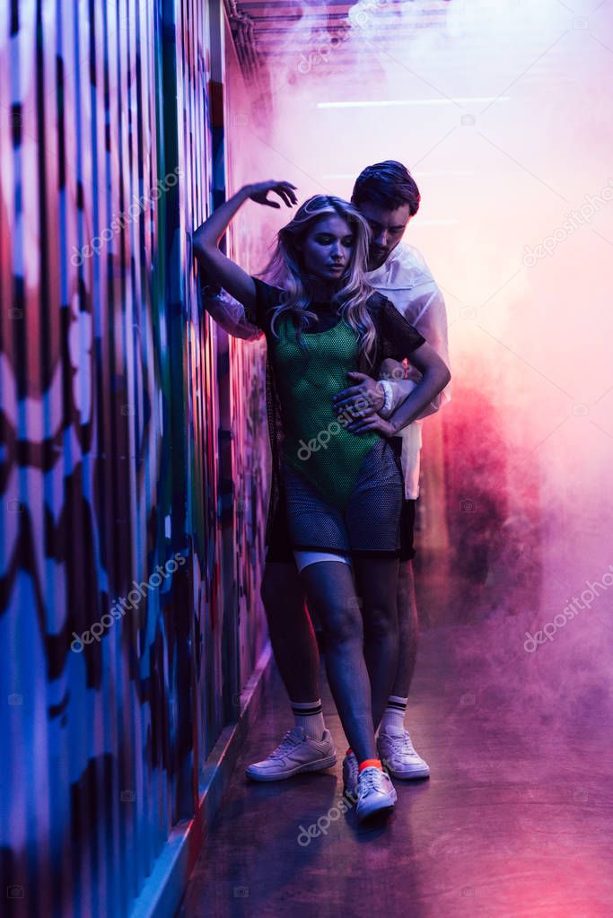 attractive and blonde woman hugging with handsome man near wall 