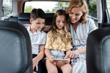 selective focus of cheerful mother pointing with finger at smartphone near kids in car  clipart