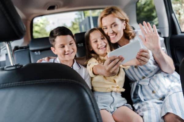 selective focus of happy family taking selfie on smartphone in car 