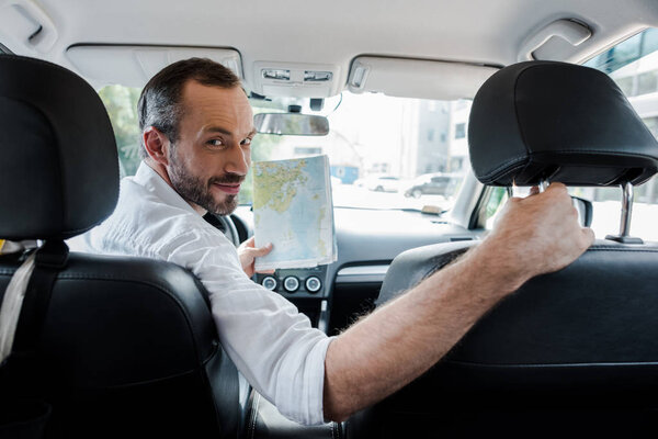 selective focus of bearded man sitting in car and holding map 