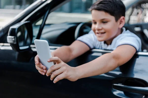 車の中でスマートフォンで自分撮りを取る幸せな子供の選択的な焦点 — ストック写真