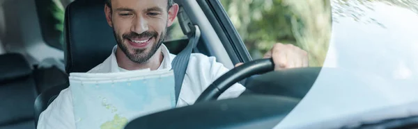 車の中に座って地図を見て幸せなドライバーのパノラマショット — ストック写真