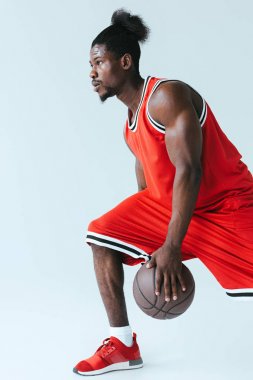 Afrika Amerikan sporcu uzakta gri arka plan üzerinde basketbol oynarken bakıyor