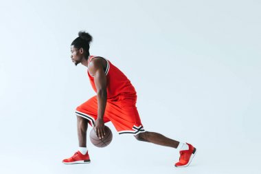 Kırmızı sporda Afrikalı Amerikan sporcu gri arka planda basketbol oynuyor