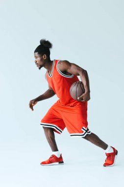 Kırmızı sporda Afrikalı Amerikan sporcu gri arka planda basketbol oynuyor