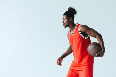 African American basketbol oyuncu tutan top ve uzak gri üzerinde izole bakıyor