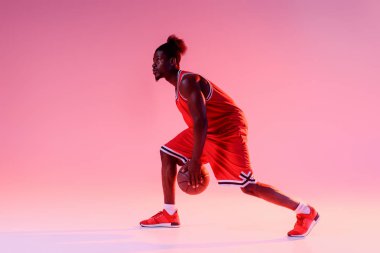 degrade ve aydınlatma ile pembe arka planda basketbol oynayan yakışıklı Afrikalı Amerikan sporcu