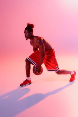 kaslı gövde ile yumuşak Afrikalı Amerikan sporcu degrade ve aydınlatma ile pembe arka planda basketbol oynuyor 