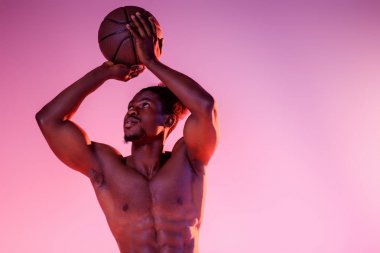 pembe ve mor degrade arka planda basketbol oynayan kaslı gövde ile yakışıklı Afrikalı Amerikan sporcu