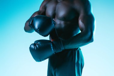 mavi arka planda boks eldiven içinde gömleksiz, kaslı Afrikalı Amerikan sporcu kırpılmış görünümü