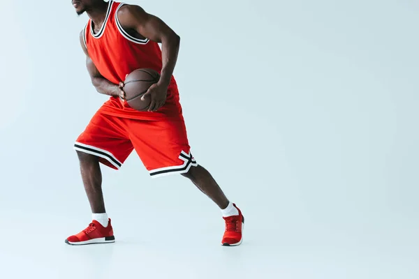 灰色の背景にバスケットボールをプレイ赤いスポーツウェアのアフリカ系アメリカ人スポーツマンの部分的なビュー — ストック写真