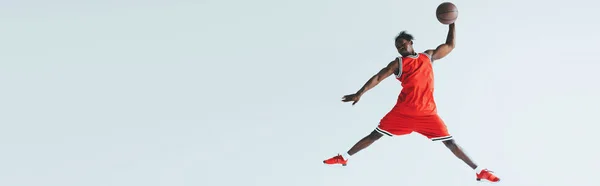 灰色で隔離されたバスケットボールをしながら アフリカ系アメリカ人のスポーツマンがジャンプするパノラマショット — ストック写真