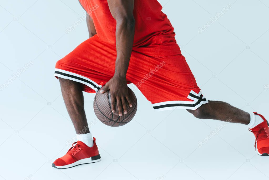 partial view of african american sportman playing basketball on grey background