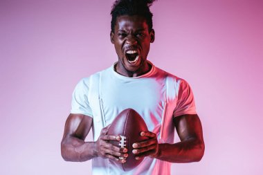 degrade ile mor arka planda Rugby topu tutarken heyecanlı African American sporcu kamera bağırıyor