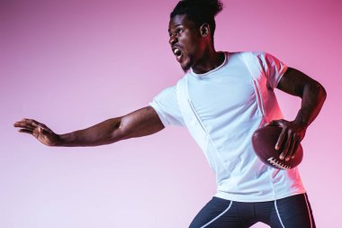heyecanlı Afrikalı Amerikan sporcu degrade ile mor arka planda Amerikan futbolu oynuyor