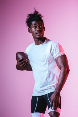 gradyan ile mor arka planda Rugby topu tutarak uzak görünümlü yakışıklı Afrikalı Amerikan sporcu