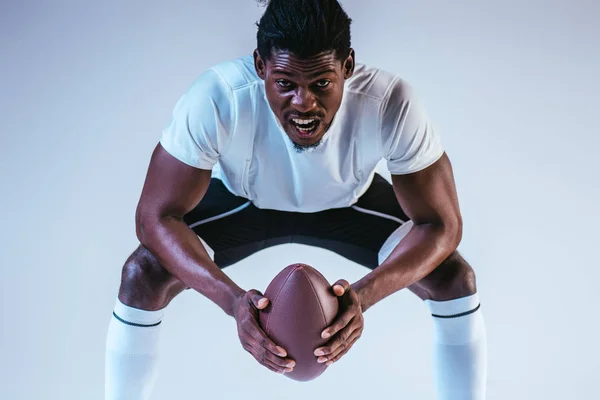 青い背景にアメリカンフットボールをプレイしながら叫ぶ興奮アフリカ系アメリカ人のスポーツマン — ストック写真