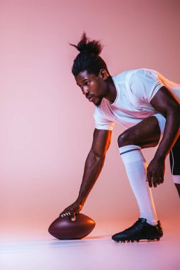 Genç Afrikalı Amerikan sporcu degrade ve aydınlatma ile pembe arka planda Amerikan futbolu oynuyor