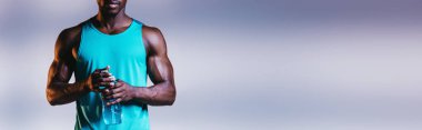 aydınlatma ile gri arka plan üzerinde kas Afrikalı Amerikan sporcu tutan spor şişesi kırpılmış görünümü, panoramik çekim