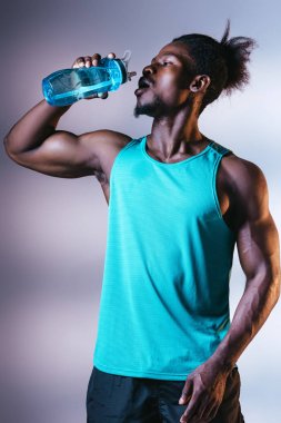 aydınlatma ile gri arka plan üzerinde spor şişesinden atletik Afrikalı Amerikan sporcu içme, yakışıklı