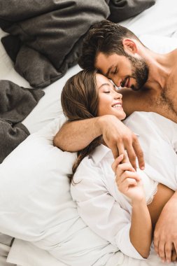 sexy young couple lying in bed, smiling with closed eyes, hugging and holding hands clipart