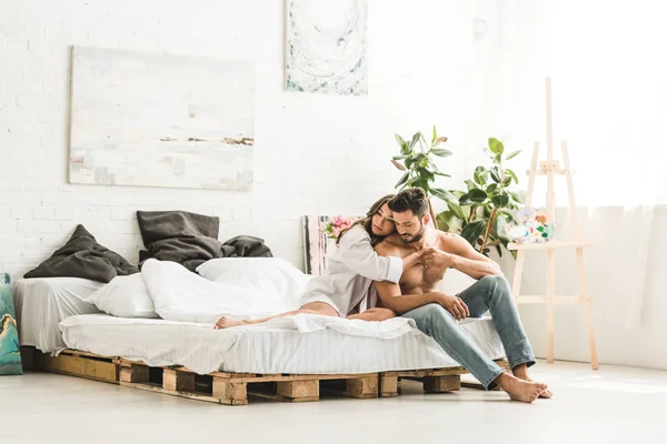 Jovem Casal Abraçando Enquanto Sentado Cama Olhando Para Longe — Fotografia de Stock