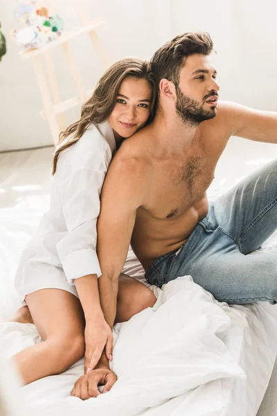 性感的夫妇坐在床上 握着手 而女孩看着相机和男人看着远 — 图库照片